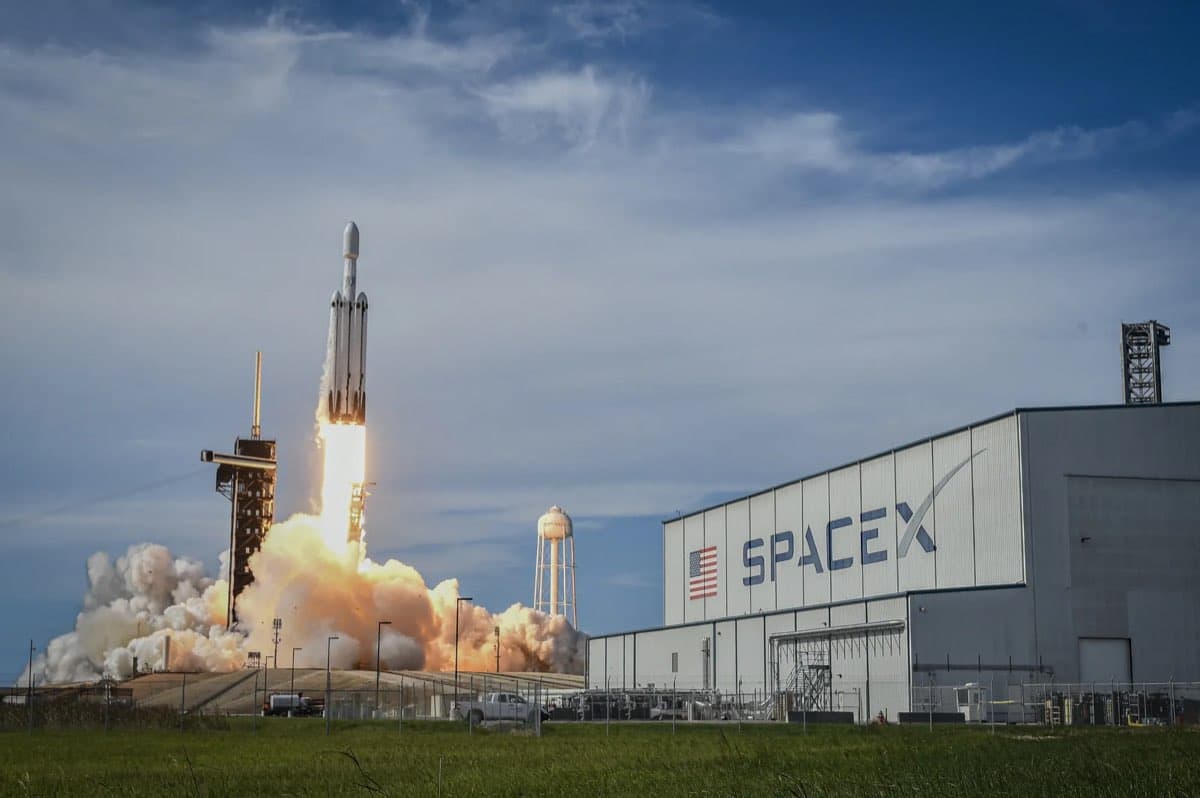 A SpaceX Falcon Heavy rocket lifts off past the SpaceX hangar